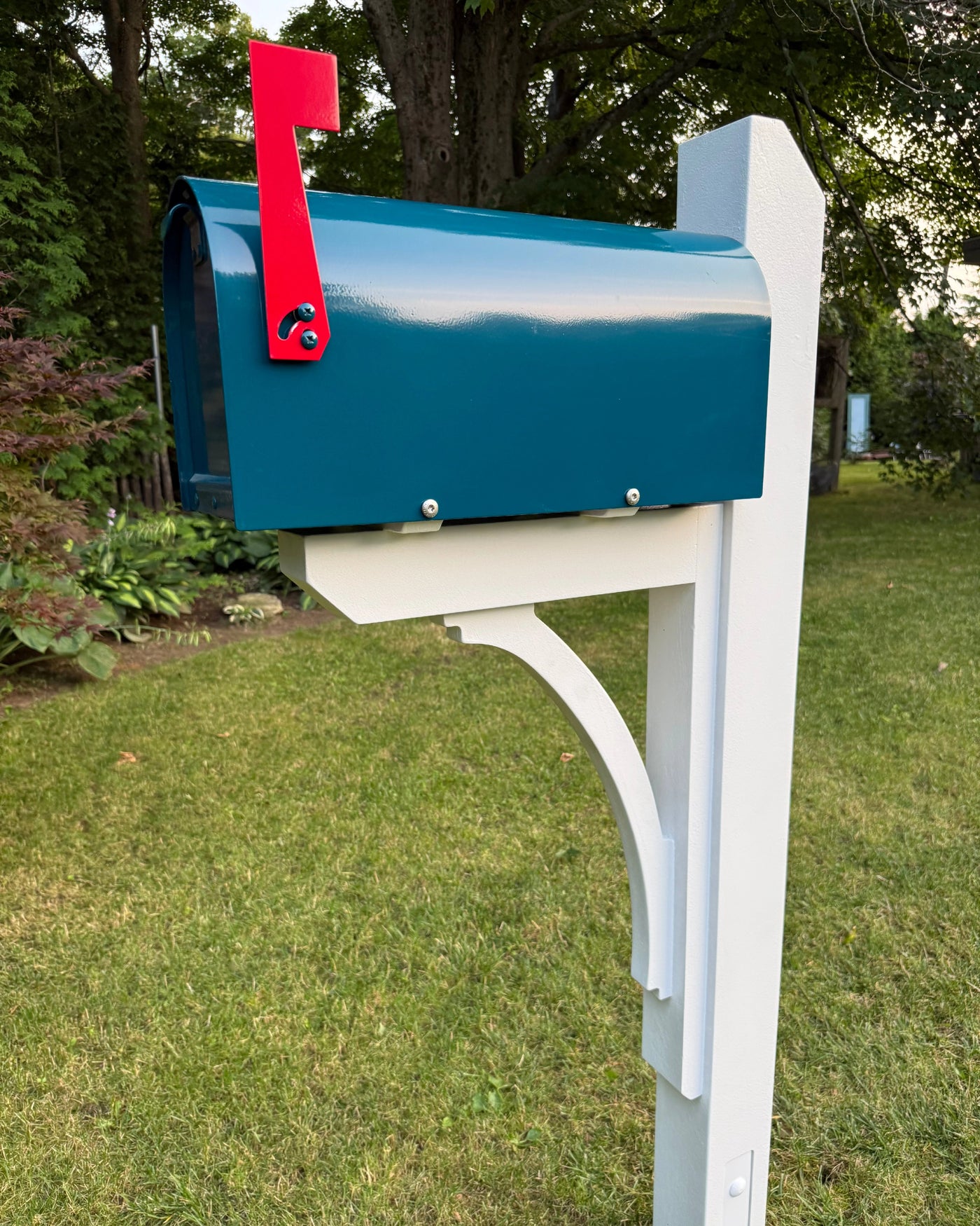 Angled front view of a teal blue mailbox set featuring a white pine post, solid cedar bracket, and bright red mailbox flag.