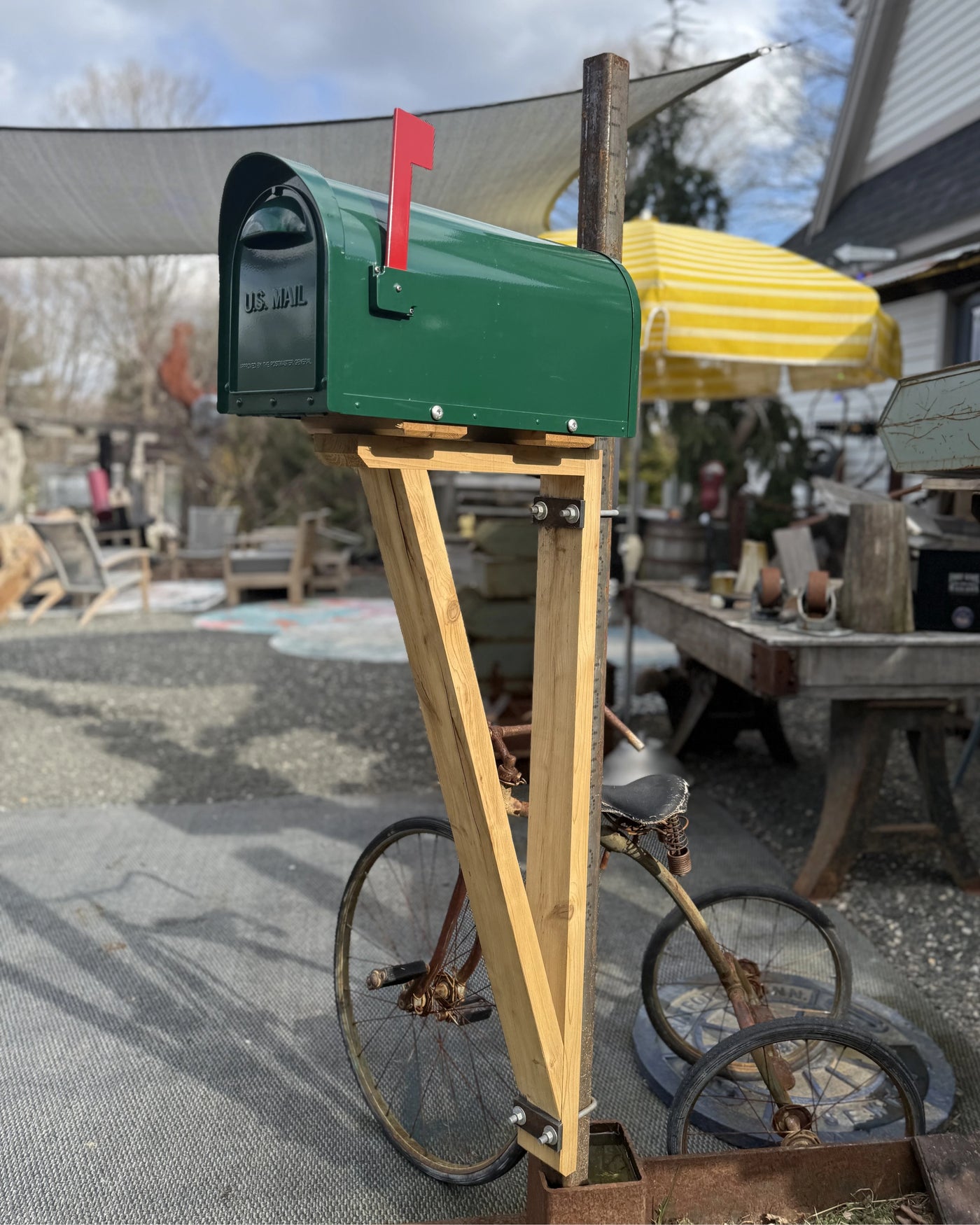 Side angle view of a green modern mailbox with natural cedar detailing and a weathered steel mounting post outdoors in natural light.