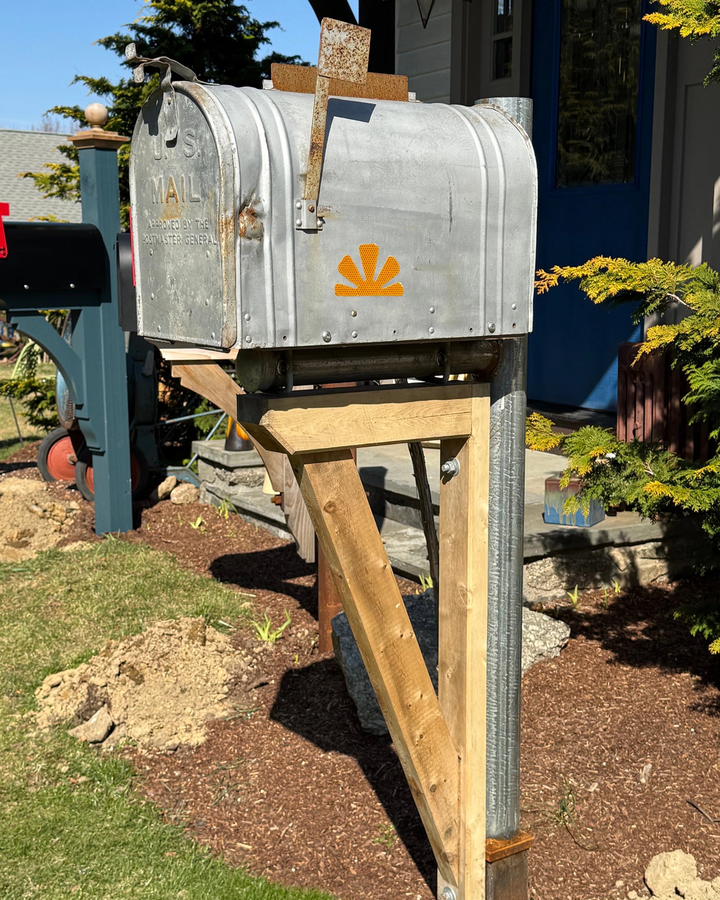 Side view of a vintage silver mailbox mounted on a galvanized steel post with a handcrafted cedar support bracket.