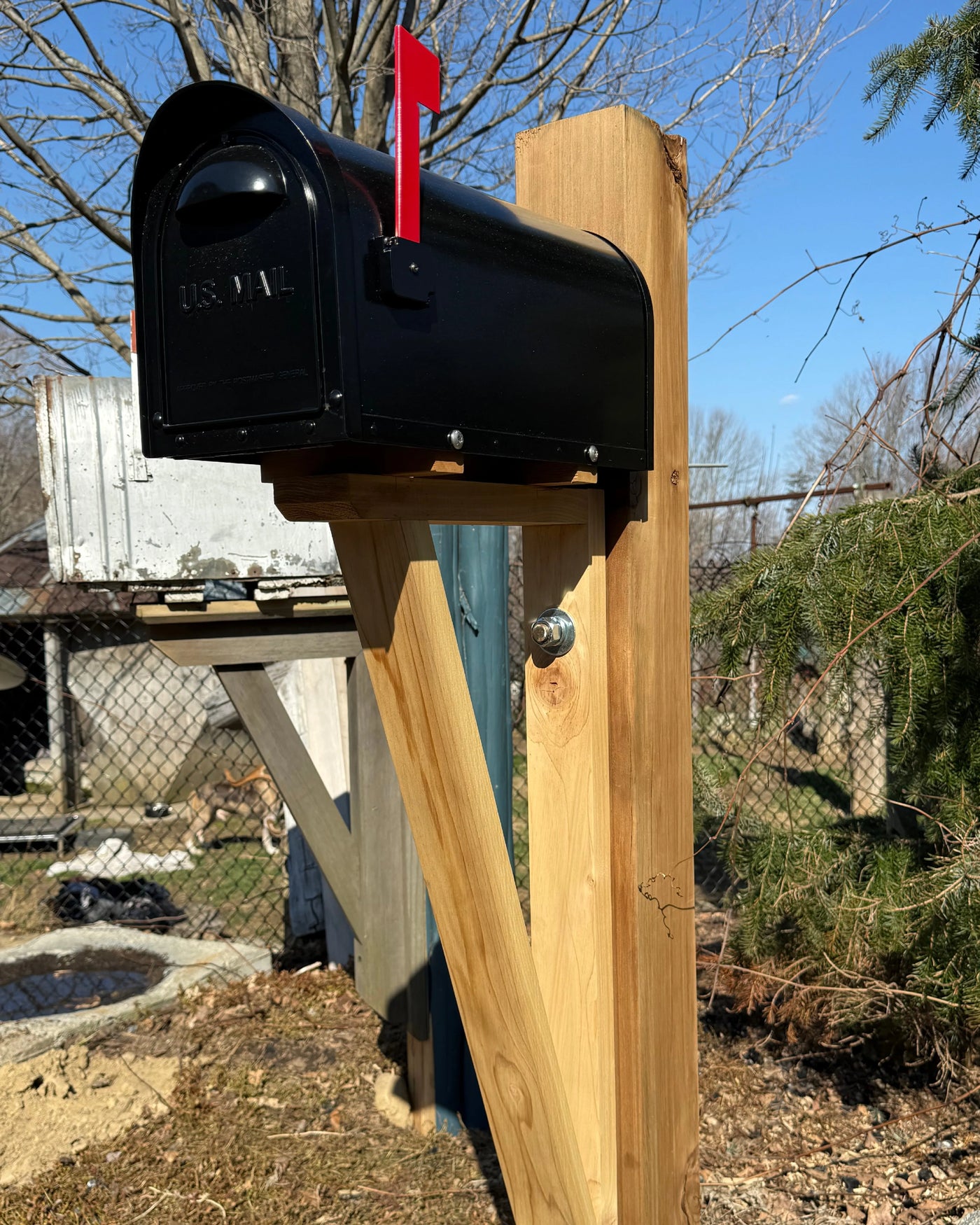 Front angled view of a black aluminum mailbox paired with a substantial red cedar post sleeved over steel.