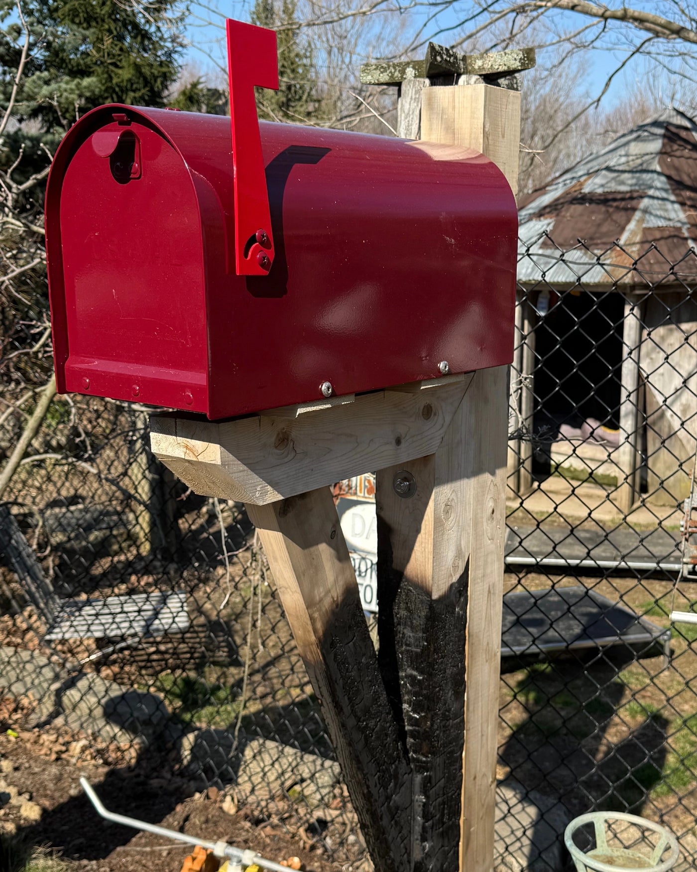 Angled view of a maroon Titan steel mailbox mounted on a cedar post with a partially charred handcrafted support bracket.
