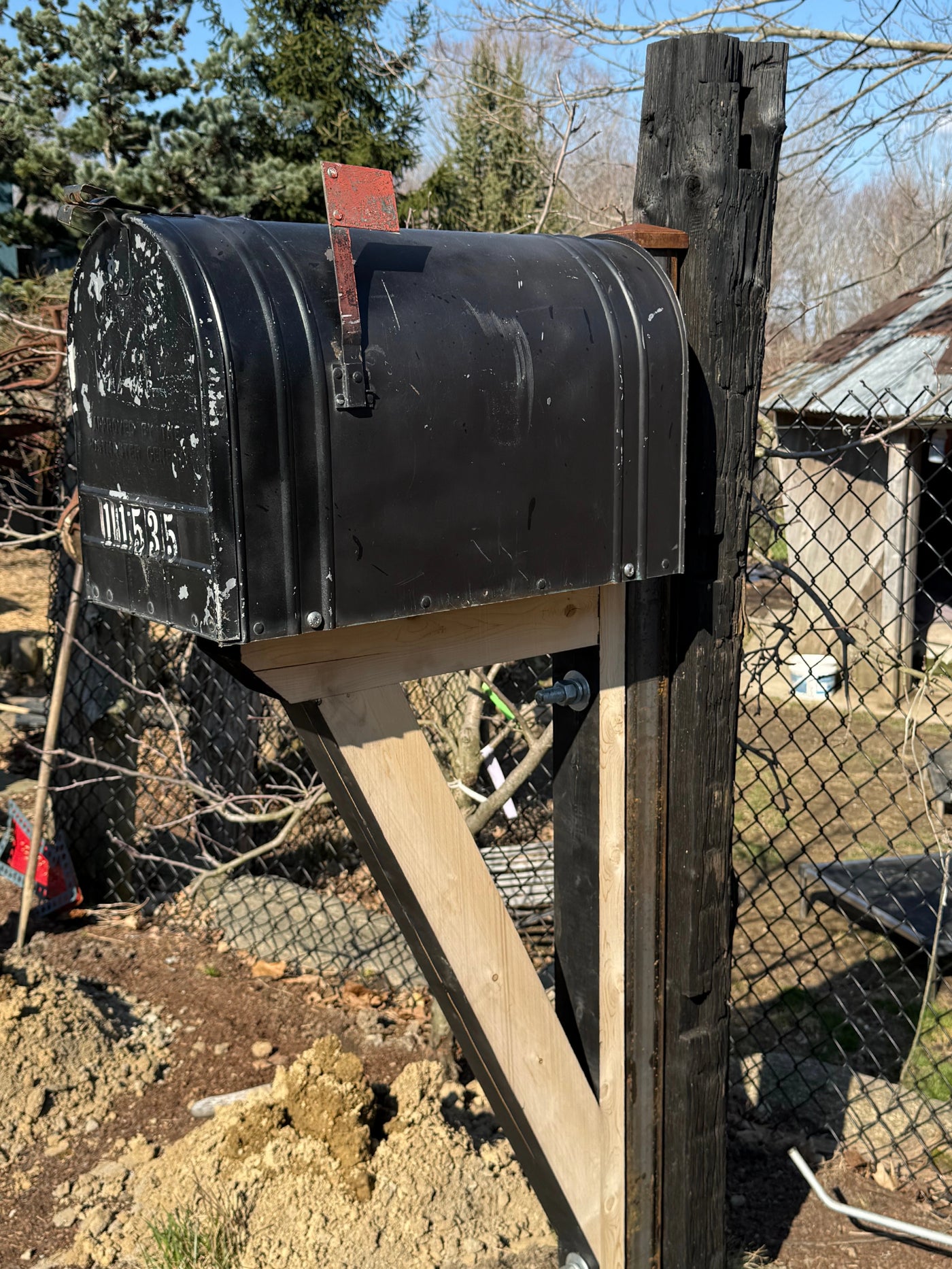 Front angled view of a distressed black vintage-style mailbox mounted on a reclaimed barn beam post with cedar bracket detailing.