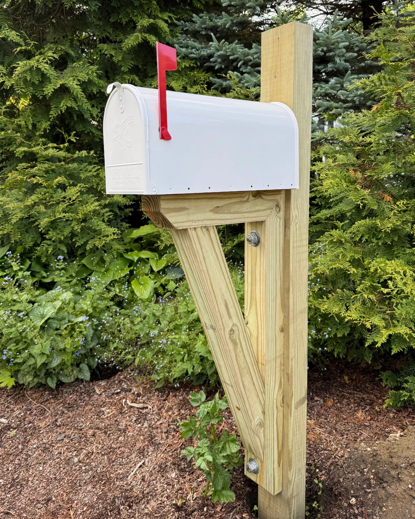 Front angled view of a black galvanized steel mailbox mounted on a pressure-treated wood post with a red mailbox flag.