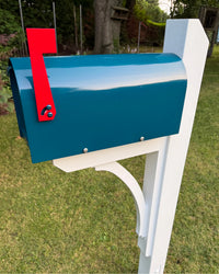 Close front side view of a teal blue mailbox with a red flag, mounted on a white pine post with a handcrafted cedar bracket.