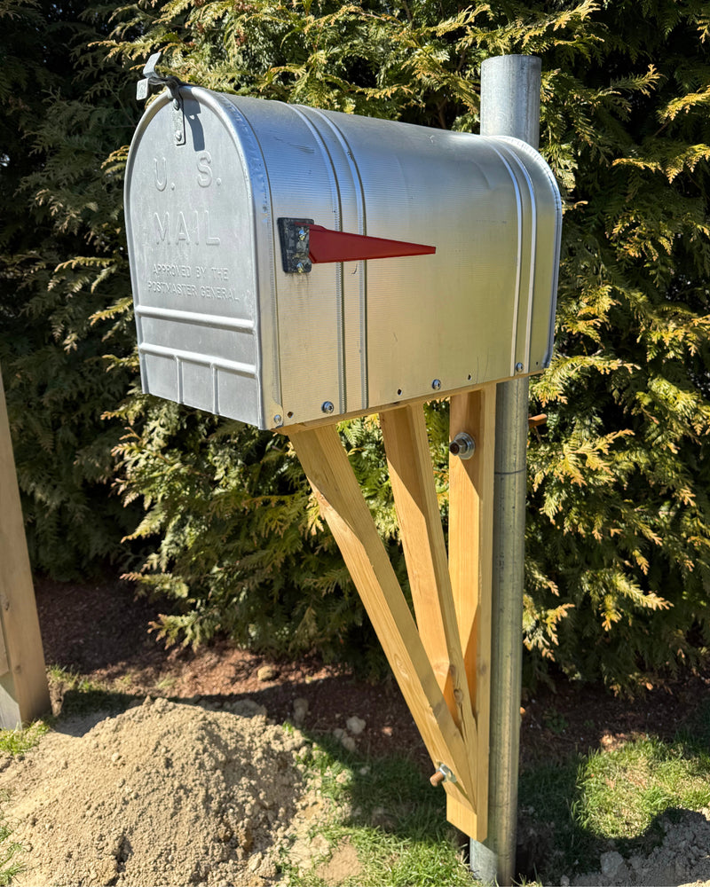 Vintage galvanized mailbox mounted on a handcrafted cedar bracket and galvanized steel post outdoors in natural sunlight.