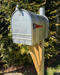Authentic vintage U.S. Mail mailbox with red flag detail, handcrafted cedar support bracket, and galvanized steel post surrounded by evergreen trees.