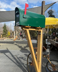 Modern green aluminum mailbox mounted on a handcrafted cedar bracket with a patina steel post and red mailbox flag.