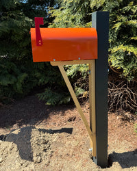 Bright orange vandal-resistant mailbox mounted on a handcrafted cedar bracket with a black steel core post outdoors in sunlight.