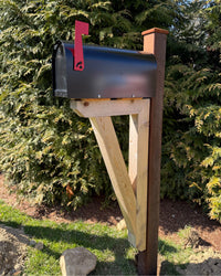 Black Titan steel mailbox mounted on a handcrafted cedar bracket with a weathered steel post and red mailbox flag outdoors.
