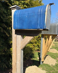 Side view of a reclaimed blue vintage mailbox with a white cedar post and custom cedar bracket in a handcrafted outdoor installation.