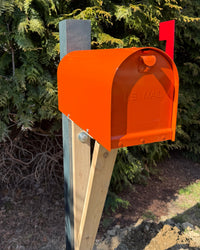 Bright orange Titan steel mailbox mounted on a handcrafted cedar bracket with a painted green post and red flag outdoors.