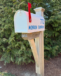 Custom white Titan steel mailbox with blue address text, red flag, and handcrafted cedar bracket designed for durable curb appeal.