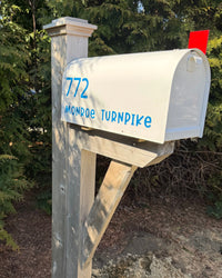 White Titan steel mailbox with blue address lettering mounted on a handcrafted white cedar post and bracket outdoors.
