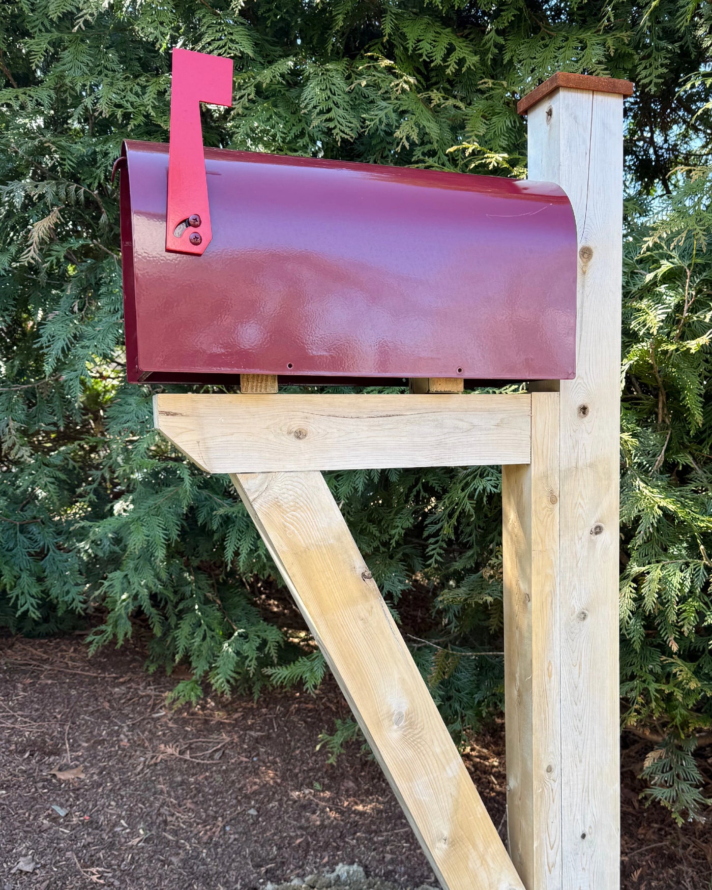 Maroon Titan steel mailbox mounted on a handcrafted white cedar post and bracket with a red flag and pyramid post cap.