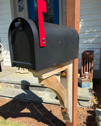 Close front view of a matte black Titan vandal-proof mailbox with cedar bracket detailing and weathered steel post.