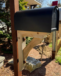 Side profile of a matte black Titan mailbox featuring a handcrafted cedar support bracket mounted to a rusted steel post.