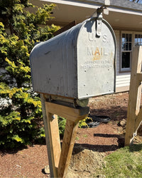 Vintage silver mailbox with rusted flag detail mounted to a galvanized steel post and cedar bracket support.