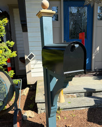 Front view of a glossy black Titan mailbox mounted on a painted blue cedar post with decorative cap detailing.
