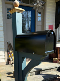 Side view of a glossy black Titan mailbox mounted on a blue painted cedar post sleeved over steel.