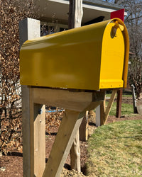 Front angled view of a yellow Titan steel mailbox paired with a white cedar post sleeved over steel.