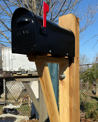 Angled view of a black aluminum mailbox mounted on a reinforced red cedar post with handcrafted cedar bracket detailing.