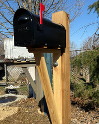 Front angled view of a black aluminum mailbox paired with a substantial red cedar post sleeved over steel.