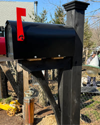 Angled view of a glossy black Titan steel mailbox mounted on a painted black cedar post with handcrafted cedar bracket detailing.