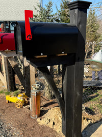 Front angled view of a glossy black Titan mailbox with a black cedar post and reinforced handcrafted bracket.