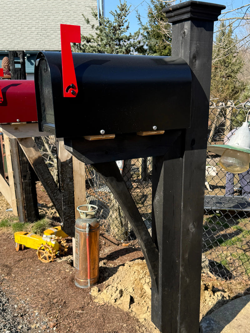 Front angled view of a glossy black Titan mailbox with a black cedar post and reinforced handcrafted bracket.