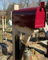 Front angled view of a maroon Titan mailbox paired with natural cedar and a partially charred cedar bracket detail.