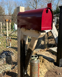 Side view of a maroon Titan steel mailbox with a handcrafted cedar bracket featuring contrasting charred wood detailing.