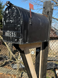 Angled view of a rustic black mailbox featuring distressed detailing and mounted to a reclaimed wood post with steel reinforcement.