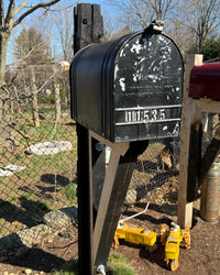 Close angled view of a vintage-inspired black mailbox with worn texture and handcrafted rustic wood post construction.