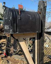 Side view of a weathered black XL mailbox paired with a stained barn beam post and handcrafted cedar support bracket.