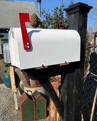 Front angled view of a white Titan steel mailbox mounted on a black-painted cedar post with matching handcrafted bracket detailing.