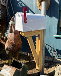 Side view of a white Titan steel mailbox mounted on a galvanized steel post with a handcrafted double cedar support bracket.
