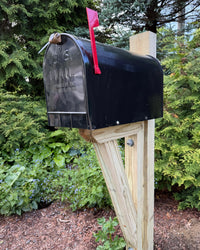 Angled view of a black architectural mailbox set featuring a pressure-treated wood structure and bright red mailbox flag.