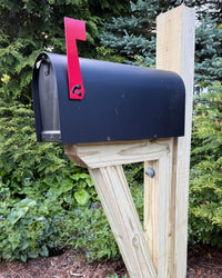 Close angled view of a black Titan steel mailbox with a red mailbox flag mounted on a pressure-treated wood post and bracket assembly.