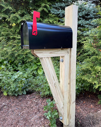 Front angled view of a black Titan steel mailbox with a red mailbox flag and handcrafted pressure-treated wood structure.