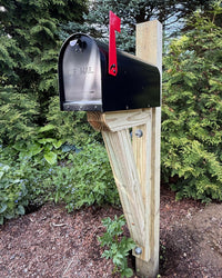 Front view of a black handcrafted mailbox set featuring a pressure-treated wood bracket and durable steel mailbox.
