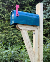 Front angled view of a teal Titan steel mailbox mounted on a pressure-treated wood post with a red mailbox flag.