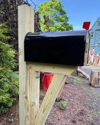 Rear side view of a black galvanized steel mailbox mounted on a pressure-treated wood post with reinforced handcrafted bracket support.