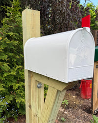 Side view of a black galvanized steel mailbox with a pressure-treated wood post and reinforced bracket assembly.
