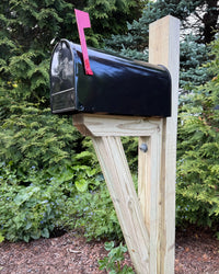 Front angled view of a white galvanized steel mailbox mounted on a pressure-treated wood post with a red mailbox flag.