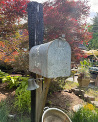 Rear side view of a distressed vintage galvanized mailbox mounted on a charred cedar post with reinforced handcrafted bracket support.