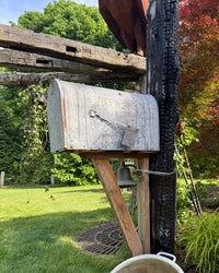 Side angled view of a weathered vintage galvanized mailbox mounted on a charred cedar post with handcrafted wood bracket and rustic bell detail.