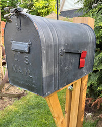 Close front view of a distressed black vintage-style mailbox mounted on a handcrafted cedar post with rustic detailing.