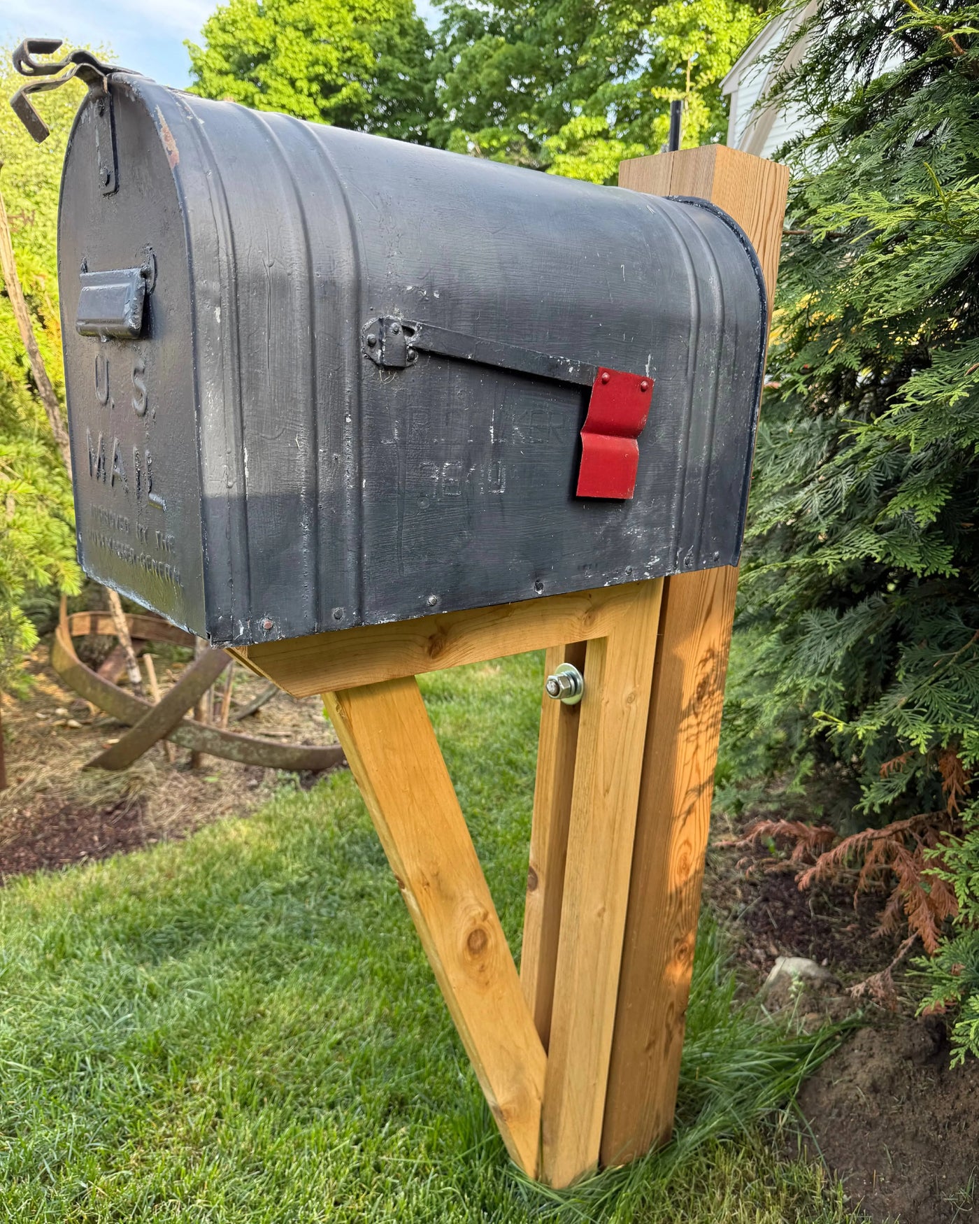 Angled side view of a distressed black vintage mailbox with red flag mounted on a handcrafted cedar post assembly.