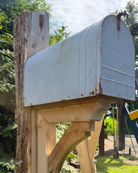 Close angled view of a weathered vintage XL mailbox mounted on a handcrafted cedar post with decorative curved bracket detail.