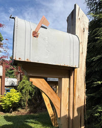 Low angle view of a vintage-style XL mailbox mounted on a handcrafted cedar support structure with natural rustic textures.